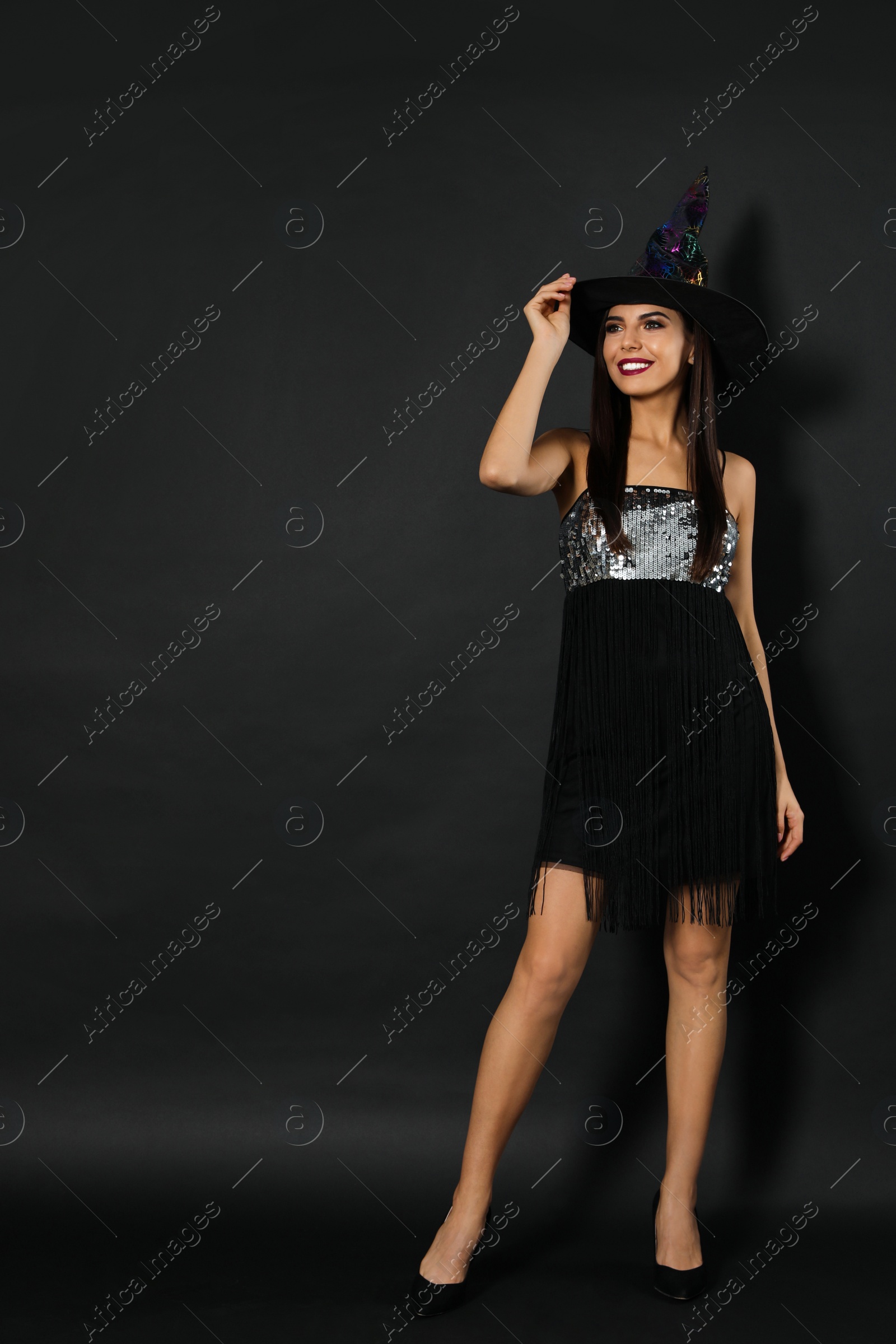 Photo of Beautiful woman wearing witch costume for Halloween party on black background, space for text