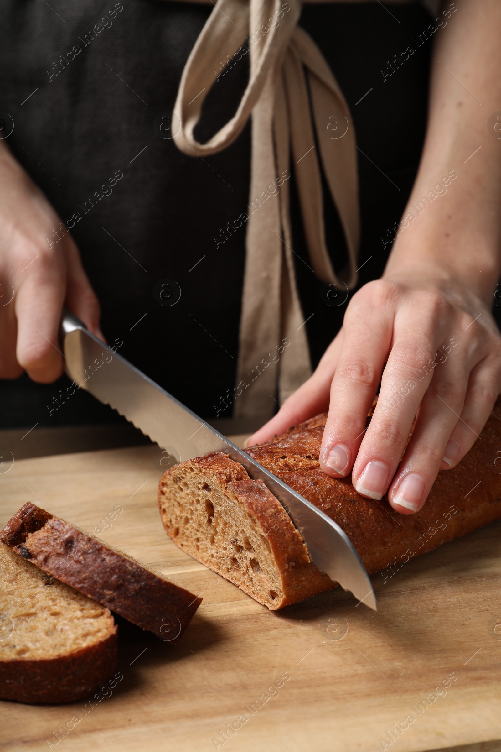 Photo of Woman cutting freshly baked rye baguette at wooden table, closeup