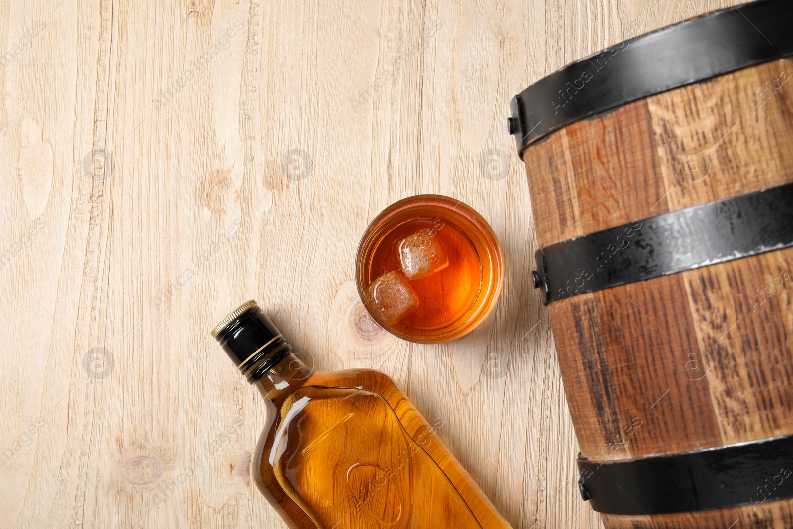 Photo of Barrel, bottle and glass of tasty whiskey on wooden table, flat lay. Space for text