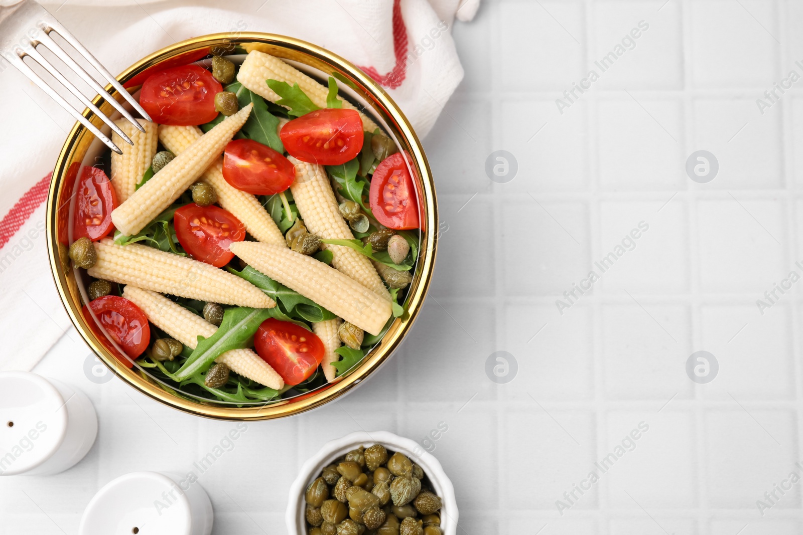 Photo of Tasty baby corn with tomatoes, arugula and capers on white tiled table, flat lay. Space for text