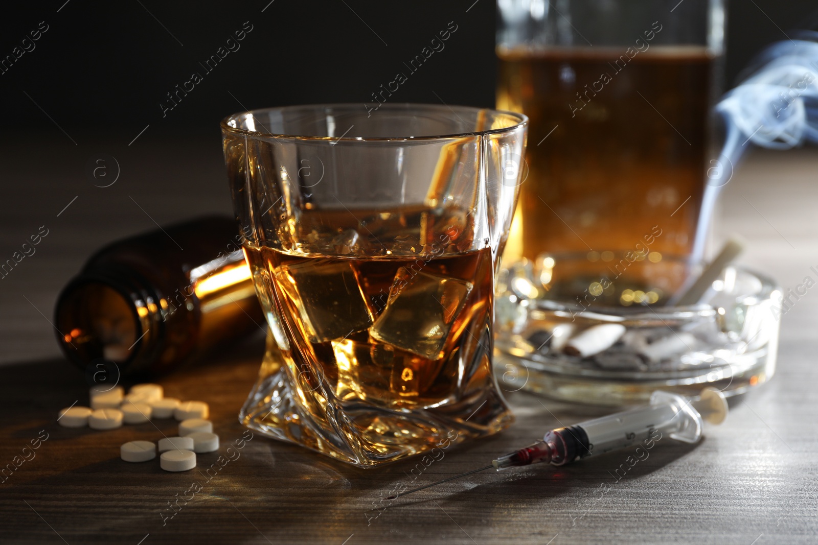 Photo of Alcohol and drug addiction. Whiskey in glass, syringe, pills and cigarettes on wooden table