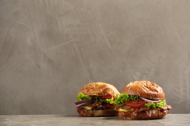 Photo of Delicious burgers with bacon on table against grey background. Space for text