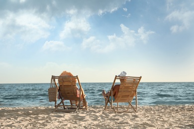 Young couple relaxing in deck chairs on beach near sea