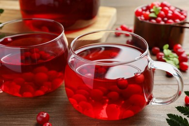 Photo of Tasty hot cranberry tea in glasses and fresh berries on wooden table