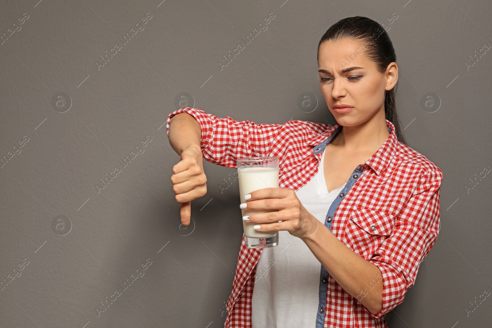 Photo of Young woman with dairy allergy holding glass of milk on grey background