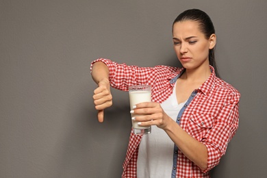 Young woman with dairy allergy holding glass of milk on grey background