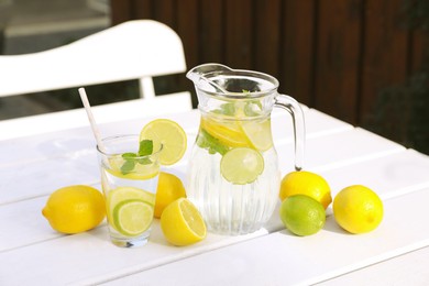 Water with lemons and limes on white wooden table outdoors