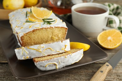 Photo of Tasty lemon cake with glaze and tea on wooden table, closeup