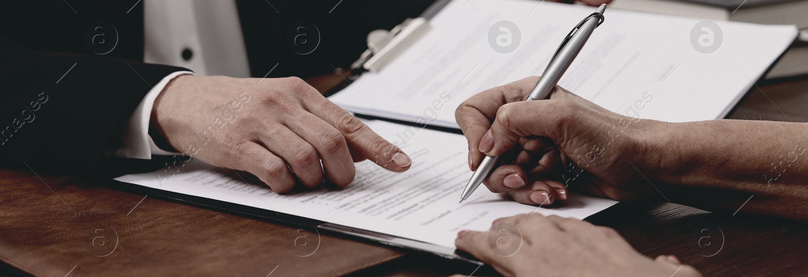 Image of Lawyer pointing at document and client putting signature at wooden table in office, closeup. Banner design