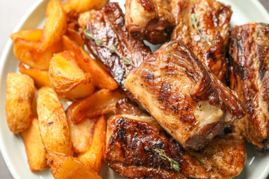 Photo of Delicious grilled ribs with potatoes on plate, closeup
