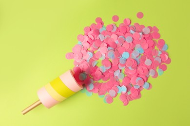 Colorful confetti bursting out of party popper on green background, flat lay