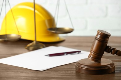 Photo of Labour, construction and land law concepts. Judge gavel, scales of justice, protective helmet, paper sheet with pen on wooden table