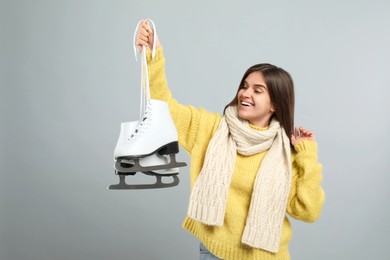 Emotional woman with ice skates on light grey background