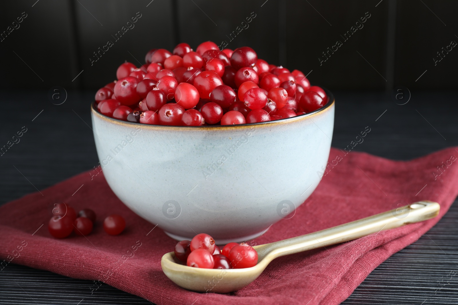 Photo of Cranberries in bowl and spoon on black wooden table, closeup