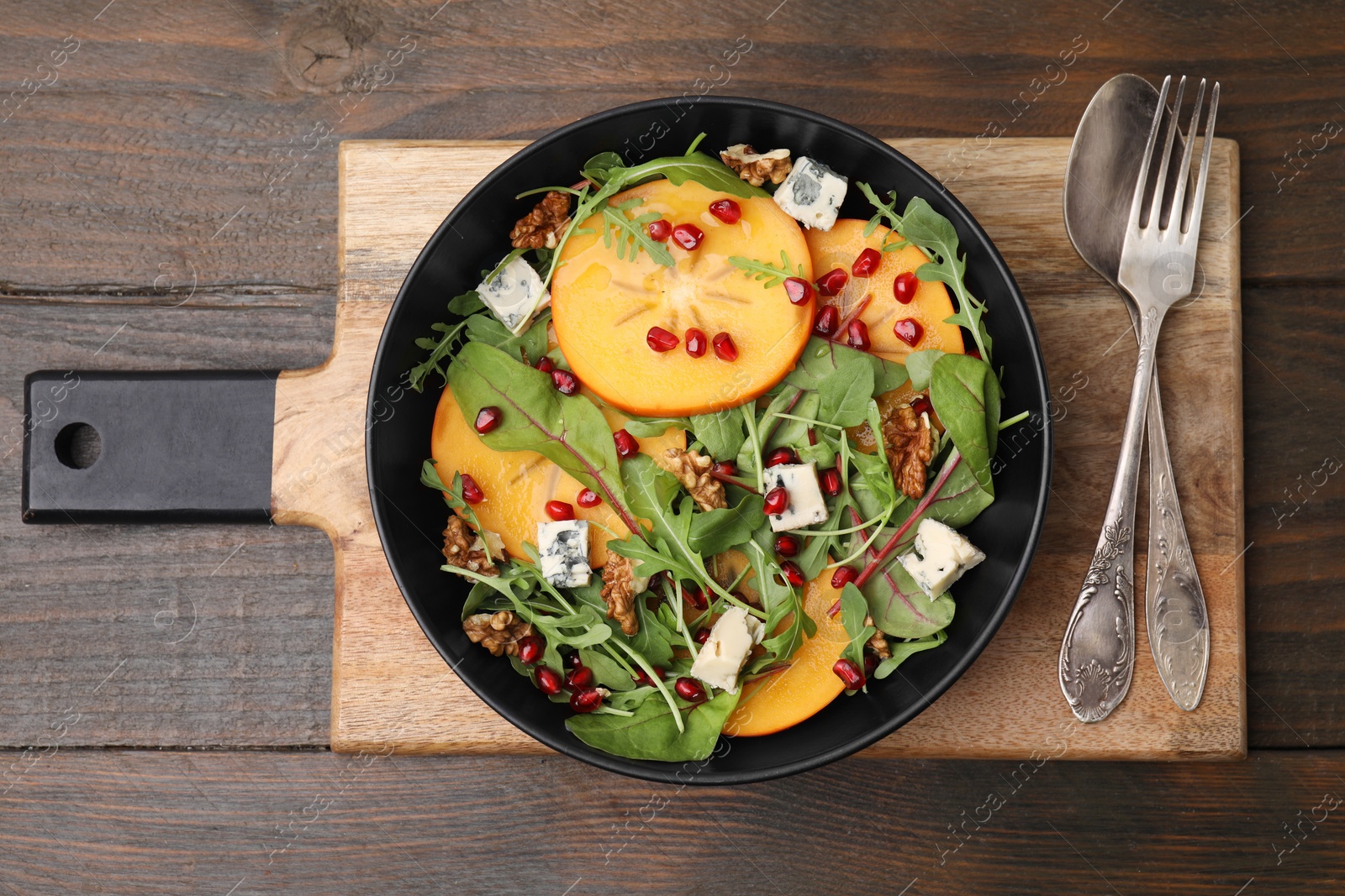 Photo of Tasty salad with persimmon, blue cheese, pomegranate and walnuts served on wooden table, top view