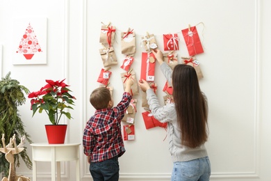 Mother and son taking gift from Advent calendar at home, back view. Christmas tradition