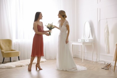 Photo of Bridesmaid giving bouquet to beautiful woman in wedding dress indoors
