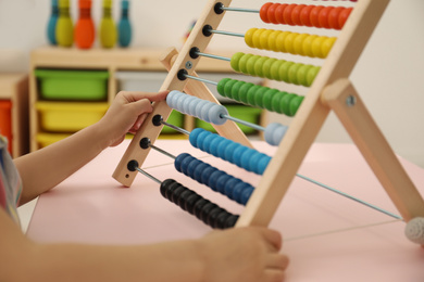 Photo of Cute child playing with wooden abacus at table in room, closeup