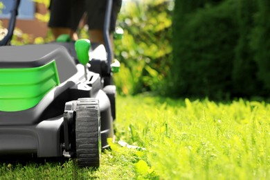 Photo of Man cutting grass with lawn mower in garden on sunny day, closeup. space for text