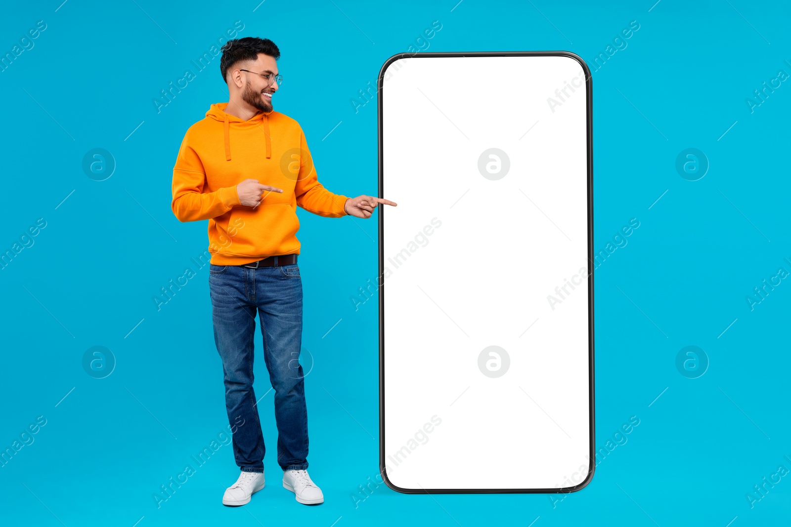 Image of Man pointing at huge mobile phone with empty screen on light blue background. Mockup for design