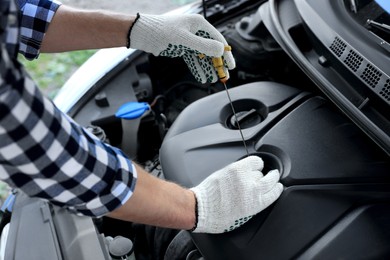 Photo of Man checking motor oil level with dipstick in car outdoors, closeup