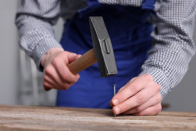 Professional repairman hammering nail into wooden board indoors, closeup