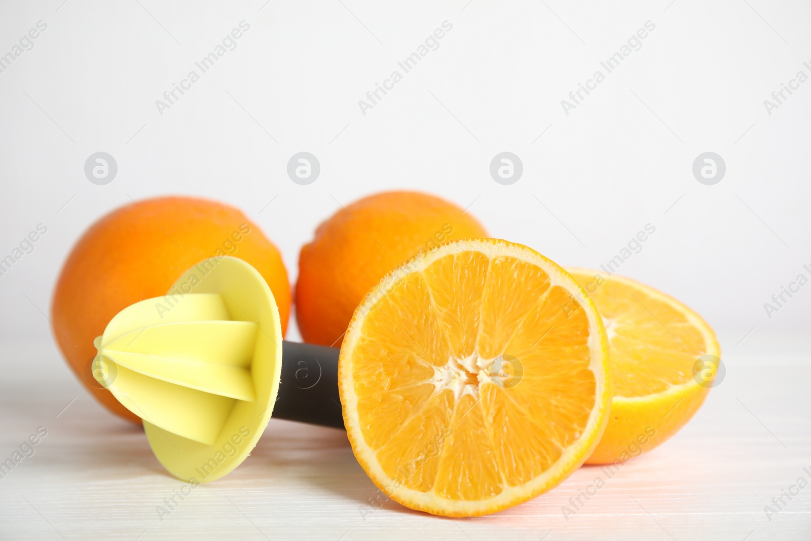 Photo of Fresh ripe oranges and reamer on white wooden table