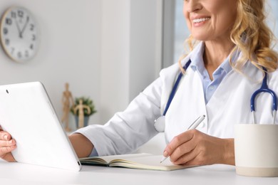Doctor with tablet and notebook at desk in clinic, closeup. Online medicine concept