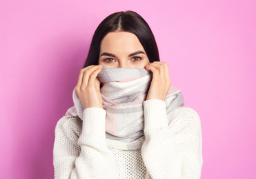 Photo of Young woman wearing warm sweater and scarf on pink background. Winter season