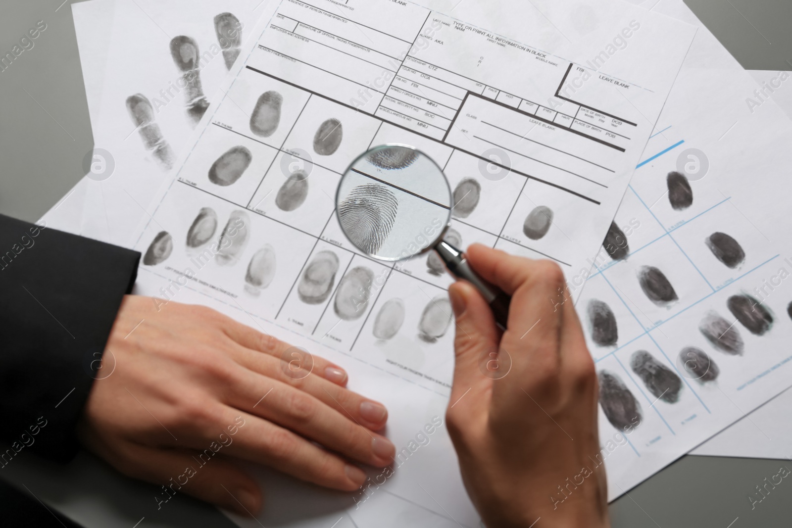 Photo of Female criminalist exploring fingerprints with magnifier at table, closeup