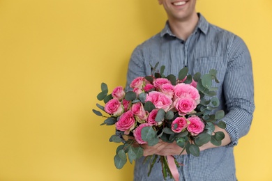 Male florist holding bouquet of beautiful flowers on color background