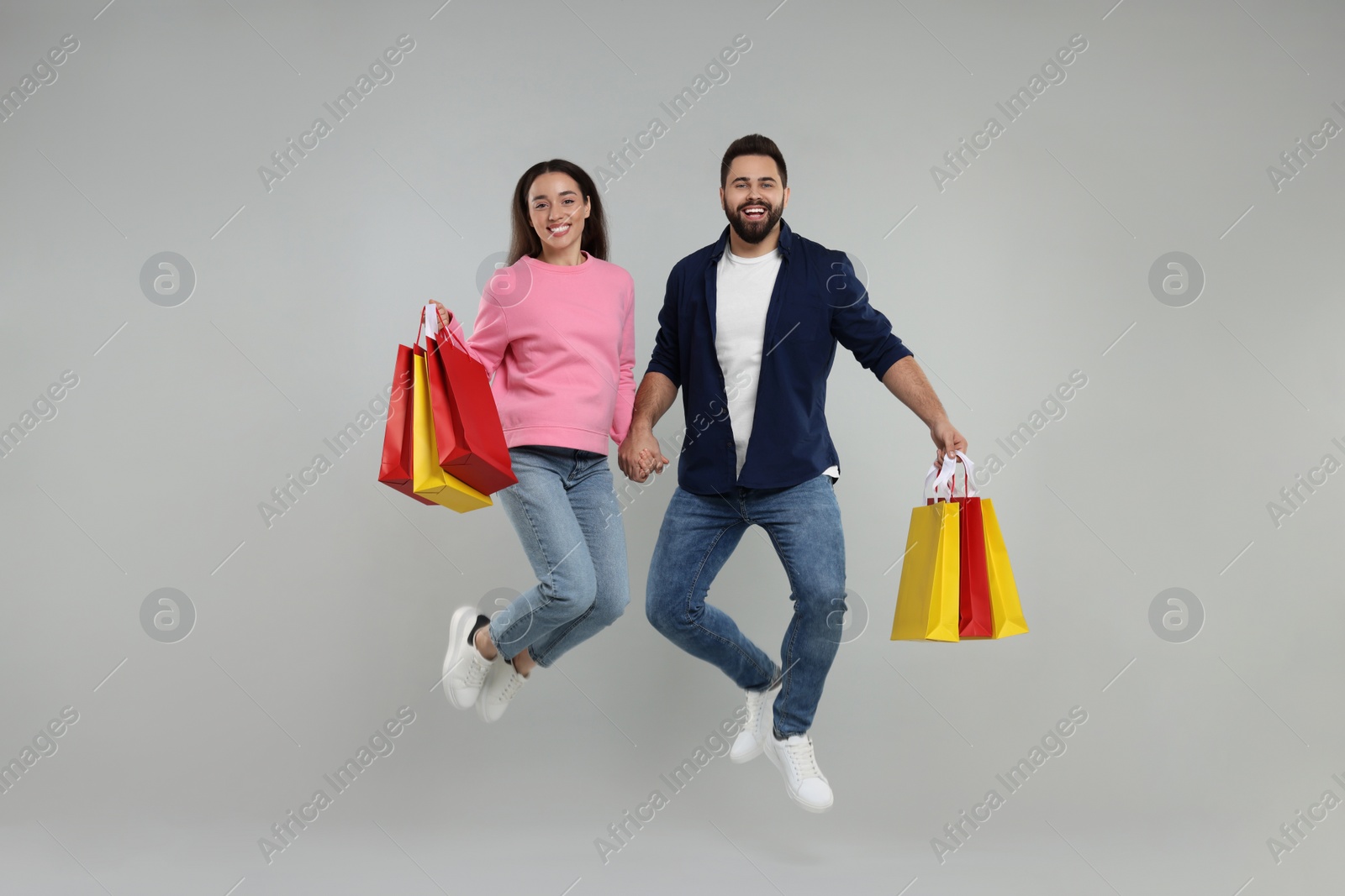 Photo of Happy couple with shopping bags jumping on grey background