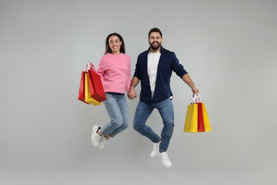 Happy couple with shopping bags jumping on grey background