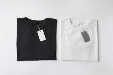 Photo of Stylish T-shirts with labels on white background, top view