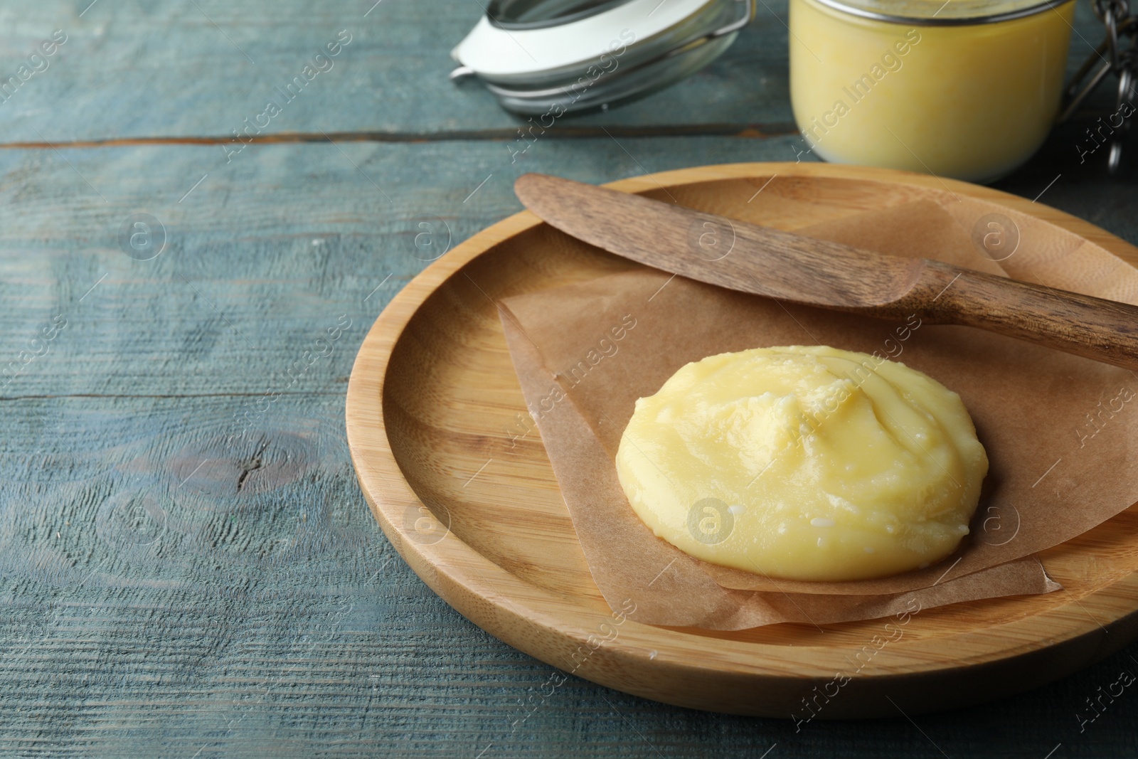 Photo of Plate and knife with Ghee butter on light blue wooden table, closeup. Space for text