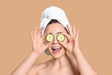 Photo of Woman with towel holding pieces of cucumber on beige background. Spa treatment