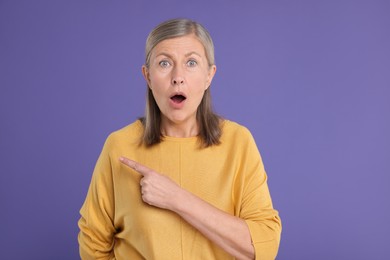 Photo of Surprised senior woman pointing at something on violet background
