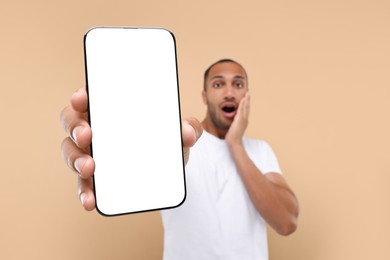 Photo of Surprised man showing smartphone in hand on beige background, selective focus. Mockup for design