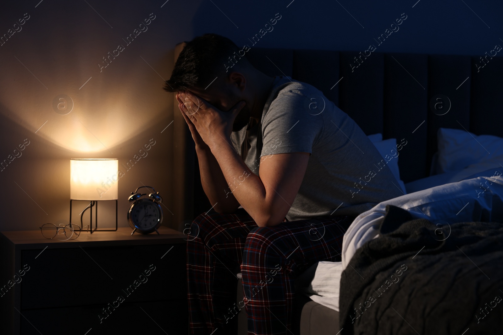 Photo of Man covering face with hands on bed