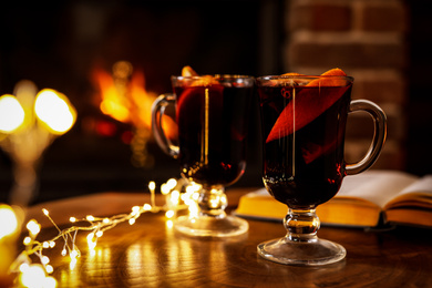 Photo of Tasty mulled wine, festive lights and blurred fireplace on background