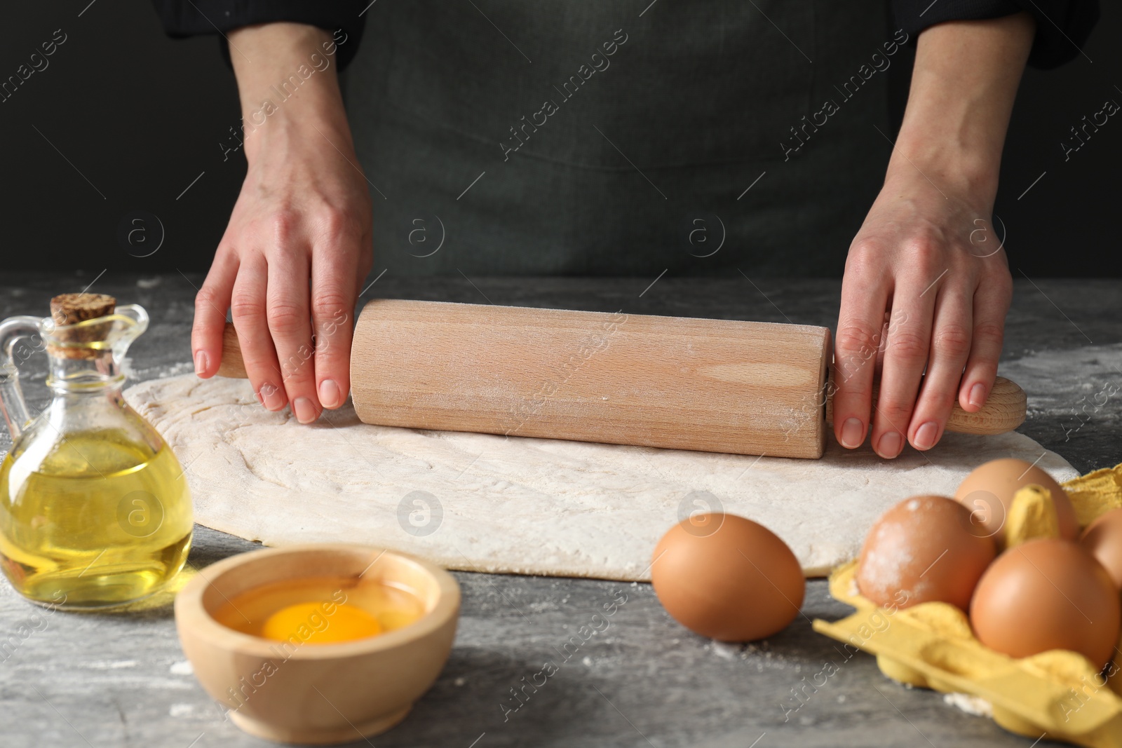 Photo of Woman rolling raw dough at grey table, closeup