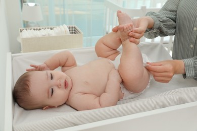 Mother changing baby's diaper on table at home