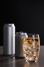 Photo of Energy drink with ice cubes in glass and aluminium cans on grey table