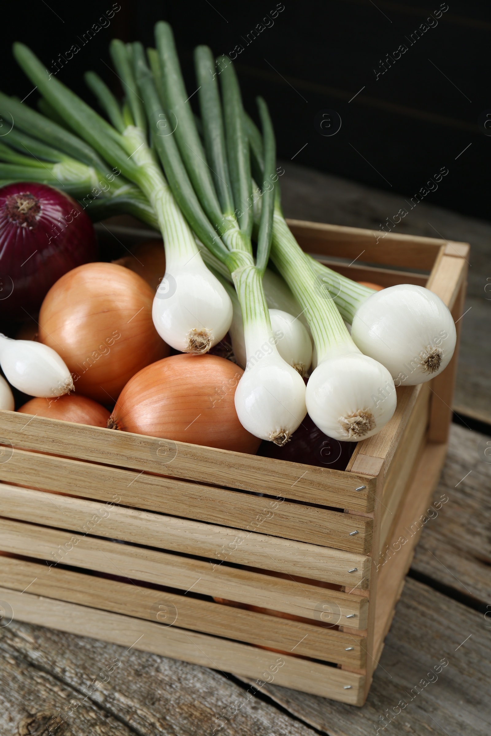 Photo of Crate with different kinds of onions on wooden table, closeup