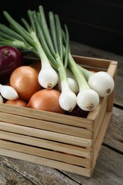 Crate with different kinds of onions on wooden table, closeup