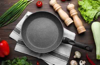 Photo of Empty frying pan, fresh vegetables and mushrooms on wooden table, flat lay
