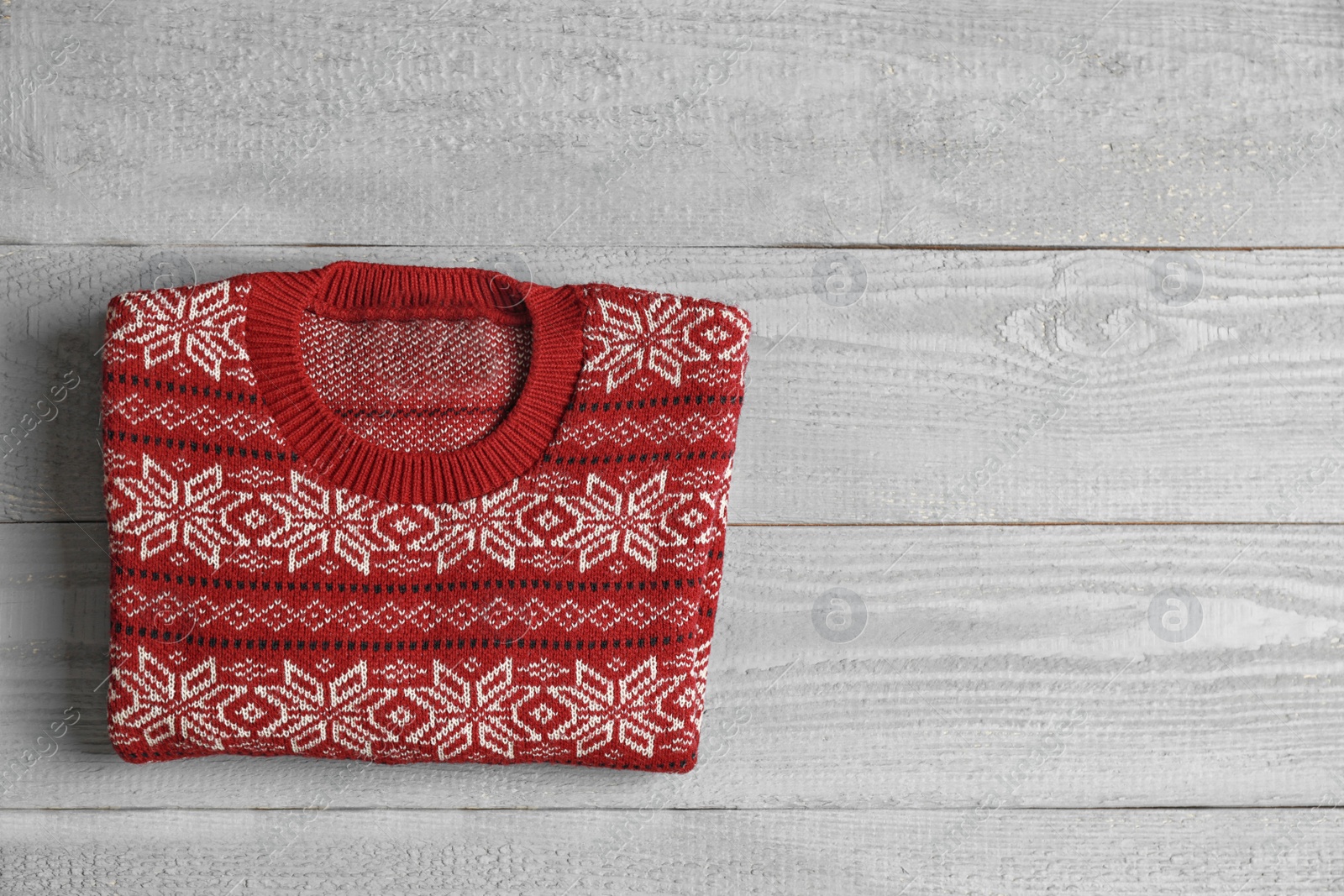 Photo of Warm folded Christmas sweater on grey wooden table, top view. Space for text