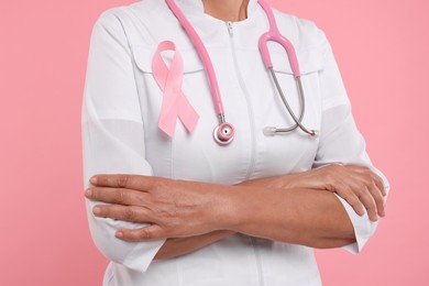Photo of Doctor with pink ribbon and stethoscope on color background, closeup. Breast cancer awareness