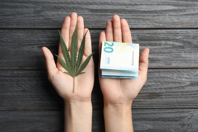 Woman holding hemp leaf and euro on grey wooden background, closeup
