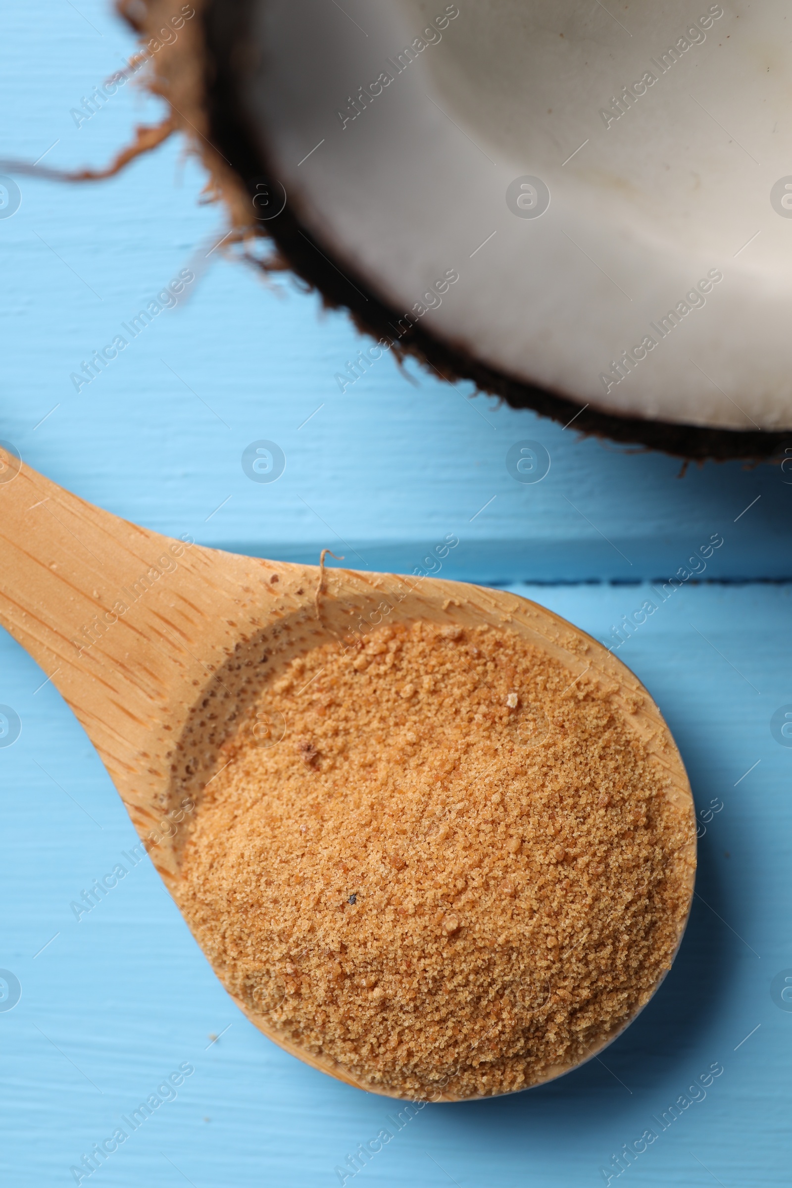 Photo of Spoon with coconut sugar and half of fruit on light blue wooden table, top view